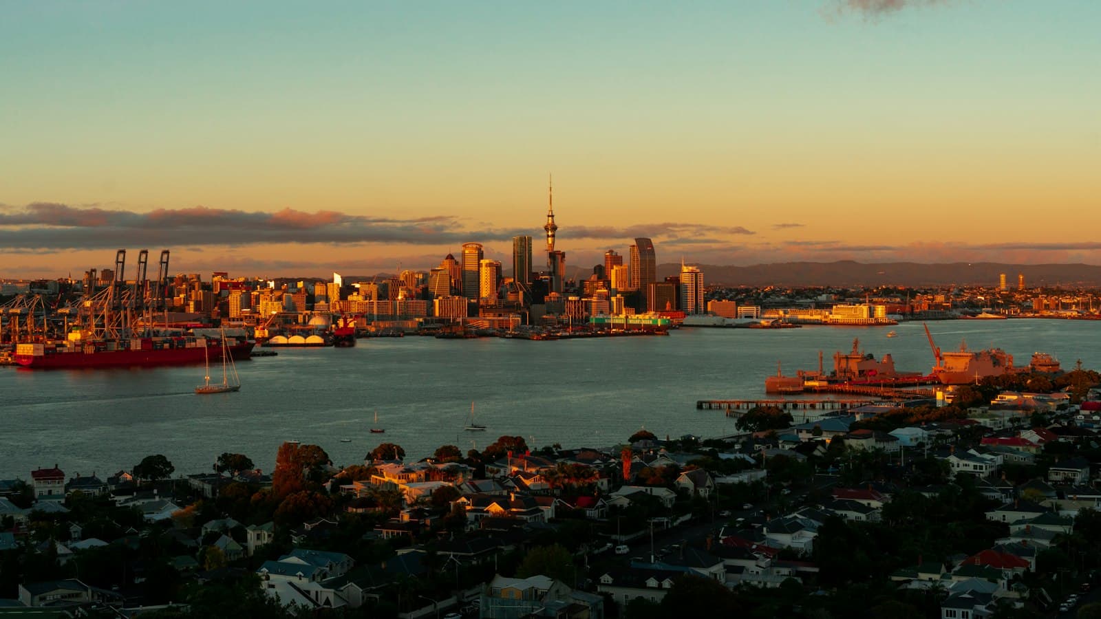 The Auckland city skyline and Sky Tower at sunset, seen across the harbour over suburban rooftops