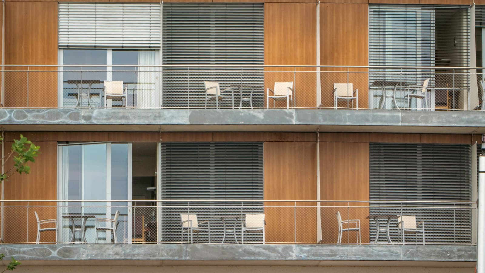 Two levels of apartment balconies with timber panels, outdoor chairs and small tables