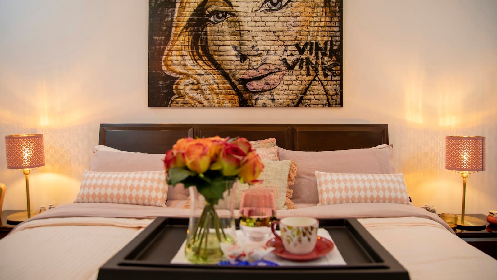 A made-up double bed with a breakfast tray of tea and roses, lit by two bedside lamps