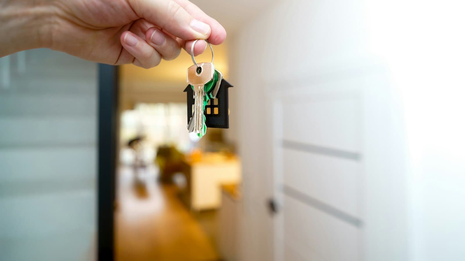 A hand holding up a set of house keys on a house-shaped keyring inside a bright home
