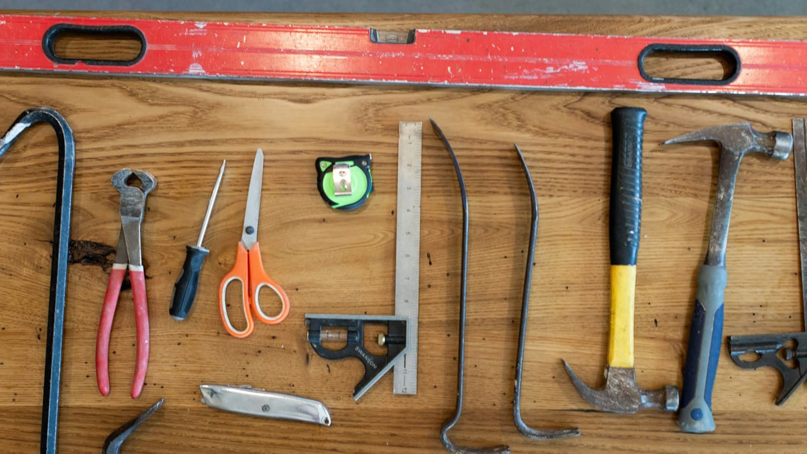 Hand tools including hammers, pliers, scissors and a set square laid out on a timber board