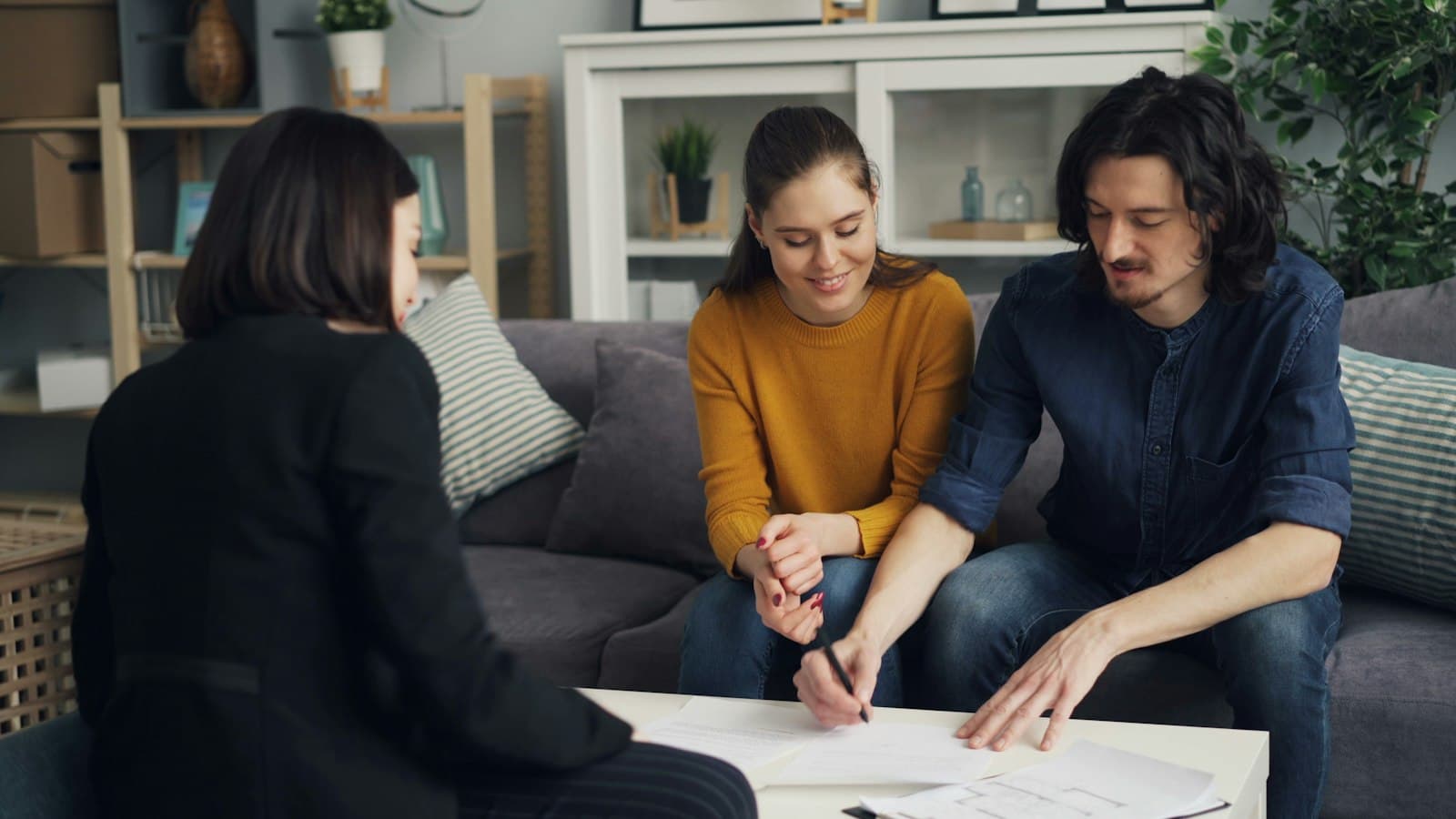 A couple on a couch signing documents with an adviser across the coffee table