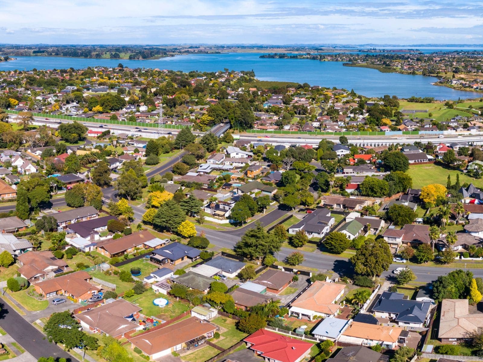 Aerial view of a South Auckland suburb of single-storey homes beside a harbour inlet